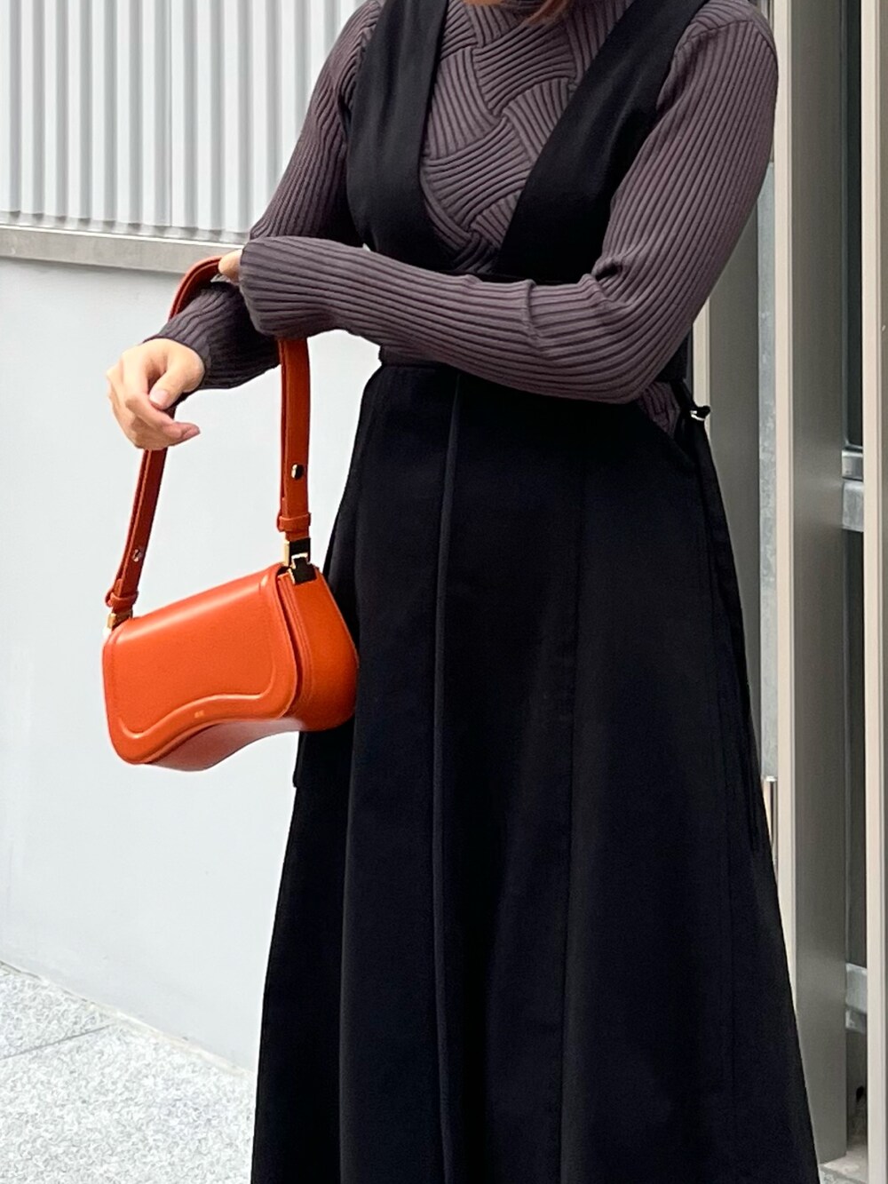 グレー系のニット/セーター、ブラック系のジャンパースカート、オレンジ系のショルダーバッグを着用したレディースの冬コーディネートの5枚目の写真