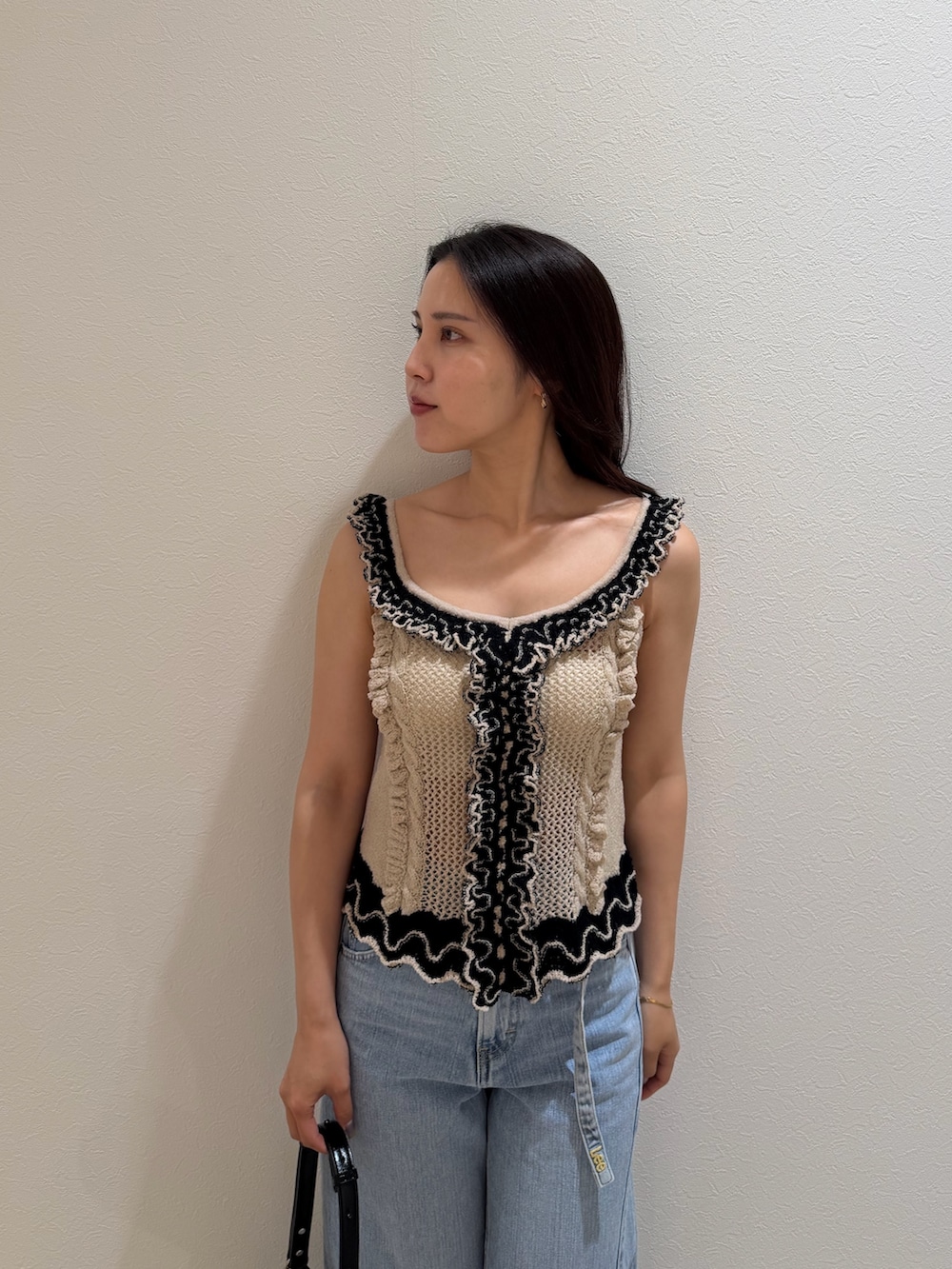ブルー系のデニムパンツ、ベージュ系のニット/セーター、ブラック系のハンドバッグを着用したレディースの夏コーディネートの4枚目の写真