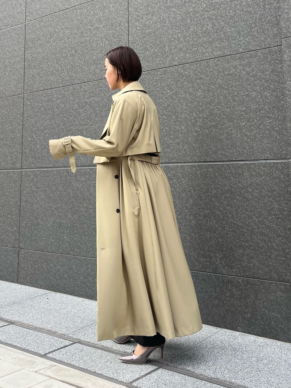 グリーン系のトレンチコート、シルバー系のパンプス、ブラック系のパンツドレスを着用したレディースの春コーディネートの3枚目の写真