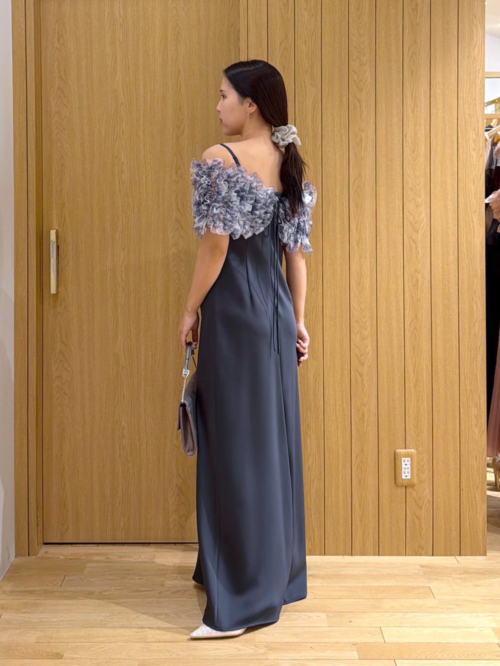 グレー系のドレス、シルバー系のクラッチバッグ、ゴールド系のパンプスを着用したレディースの秋コーディネートの2枚目の写真