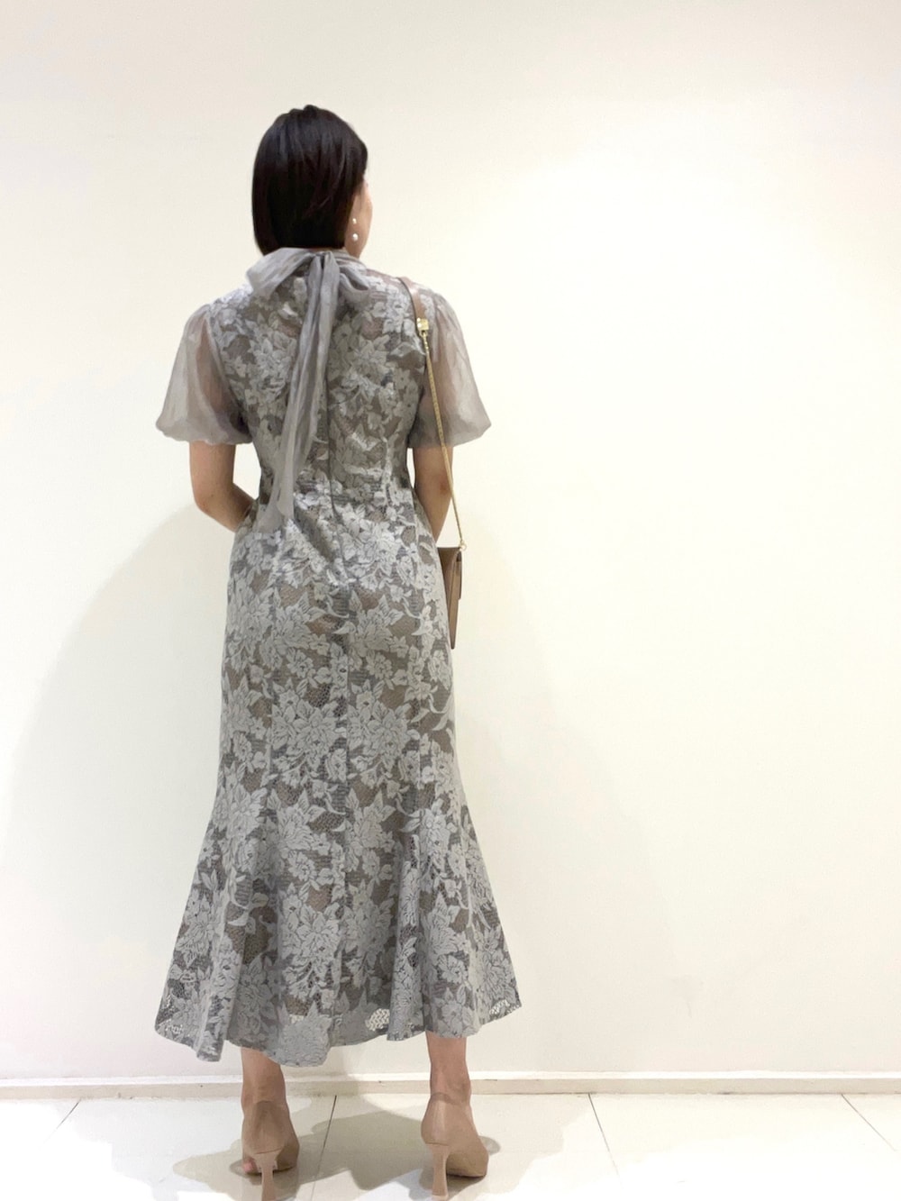 グレー系のドレス、ベージュ系のクラッチバッグ、ゴールド系のパンプスを着用したレディースの夏コーディネートの3枚目の写真