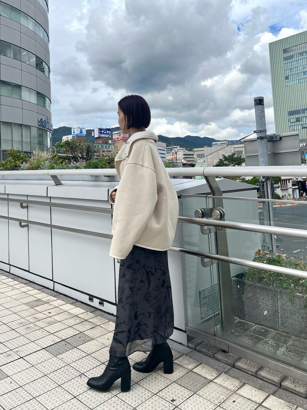 ホワイト系のムートンコート、グリーン系のニット/セーター、グレー系のスカートを着用したレディースの秋コーディネートの3枚目の写真