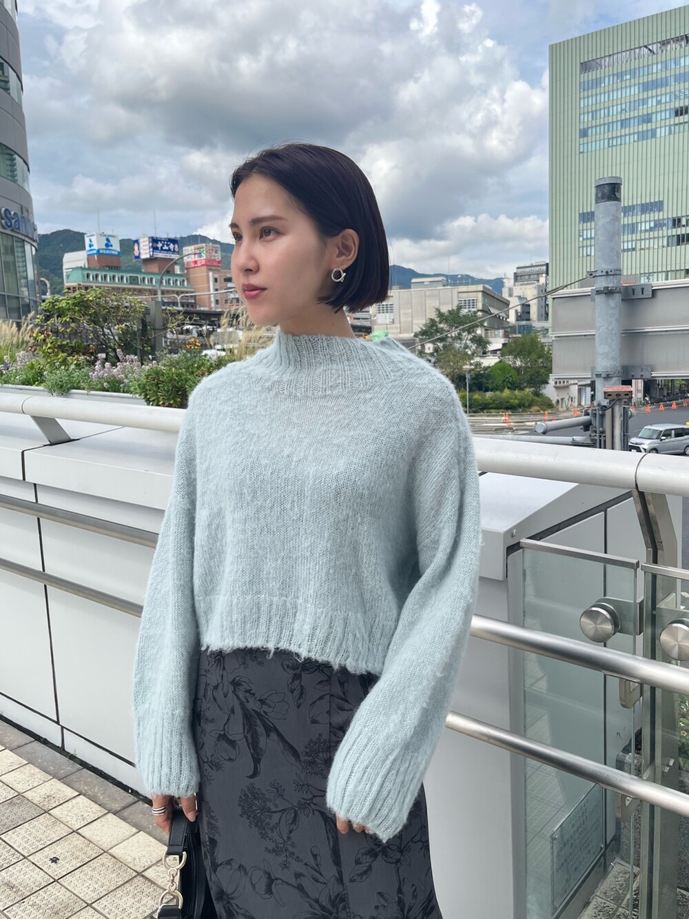 グリーン系のニット/セーター、ブラック系のハンドバッグ、グレー系のスカートを着用したレディースの秋コーディネートの5枚目の写真