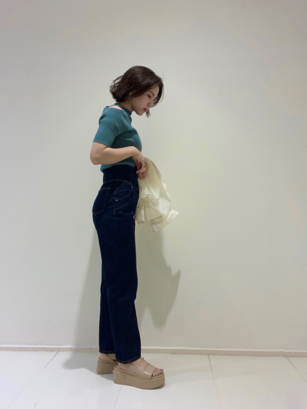 ブルー系のデニムパンツ、グリーン系のニット/セーター、ベージュ系のサンダルを着用したレディースの春コーディネートの3枚目の写真