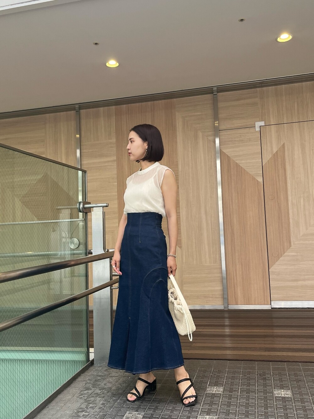 ブルー系のシャツ/ブラウス、ブルー系のデニムスカート、ベージュ系のハンドバッグを着用したレディースの夏コーディネートの4枚目の写真