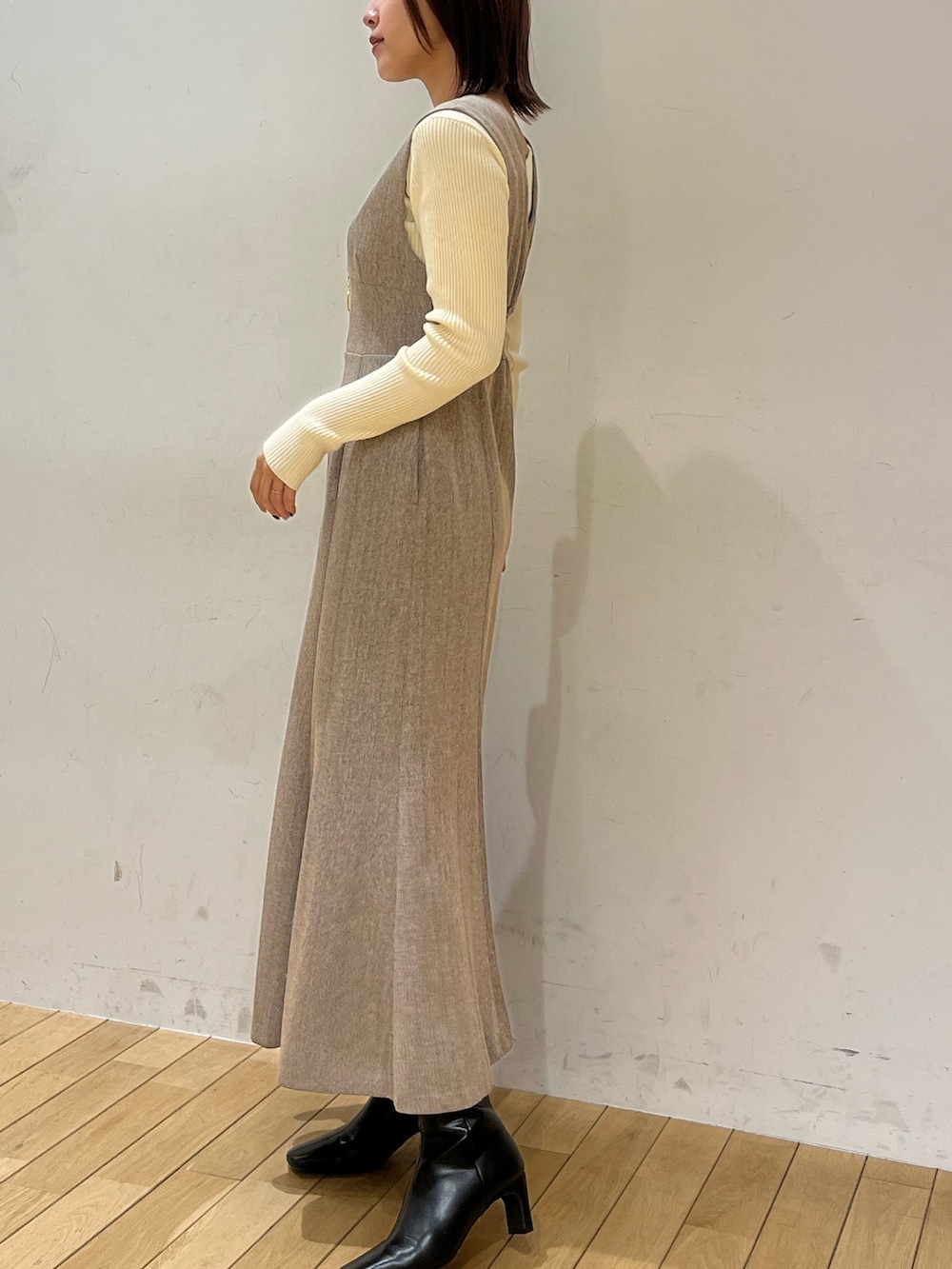 ブラック系のブーツ、ホワイト系のニット/セーター、ベージュ系のジャンパースカートを着用したレディースの冬コーディネートの2枚目の写真