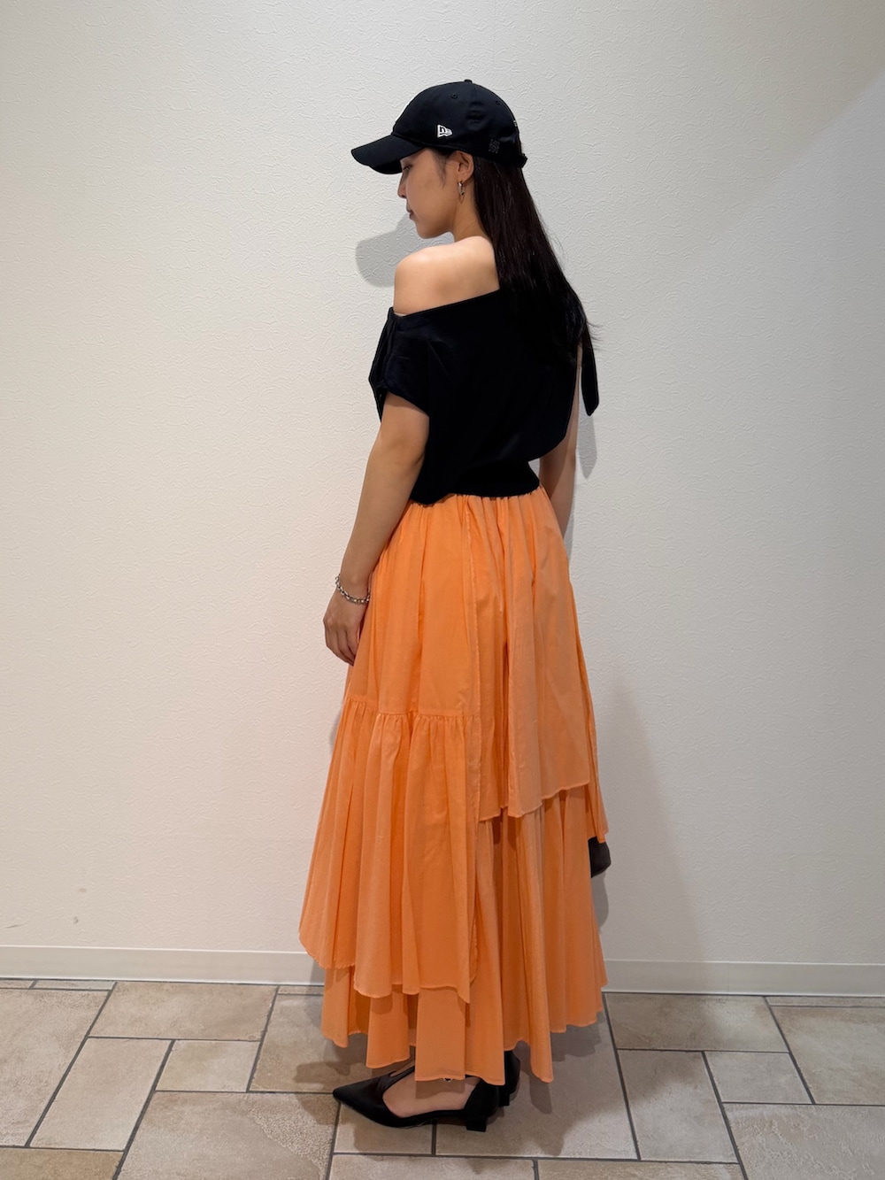 ブラック系のパンプス、ブラウン系のハンドバッグ、オレンジ系のスカートを着用したレディースの夏コーディネートの2枚目の写真