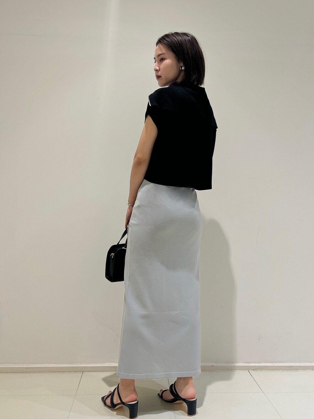 ブラック系のショルダーバッグ、ブラック系のサンダル、ブルー系のスカートを着用したレディースの春コーディネートの2枚目の写真