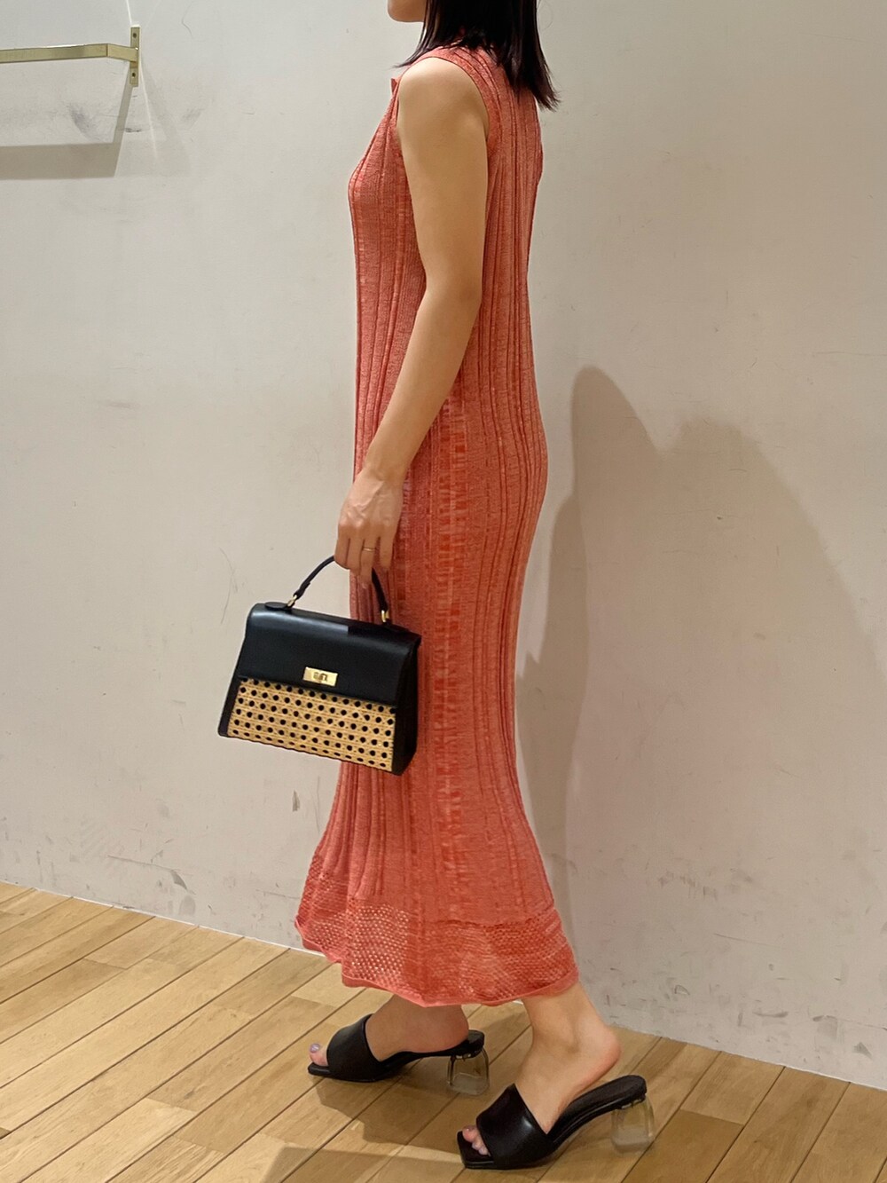 ブラック系のハンドバッグ、ブラック系のサンダル、オレンジ系のワンピースを着用したレディースの夏コーディネートの2枚目の写真