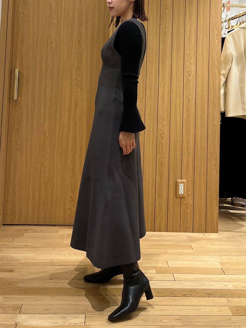 ブラック系のブーツ、ブラック系のニット/セーター、グレー系のジャンパースカートを着用したレディースの冬コーディネートの2枚目の写真