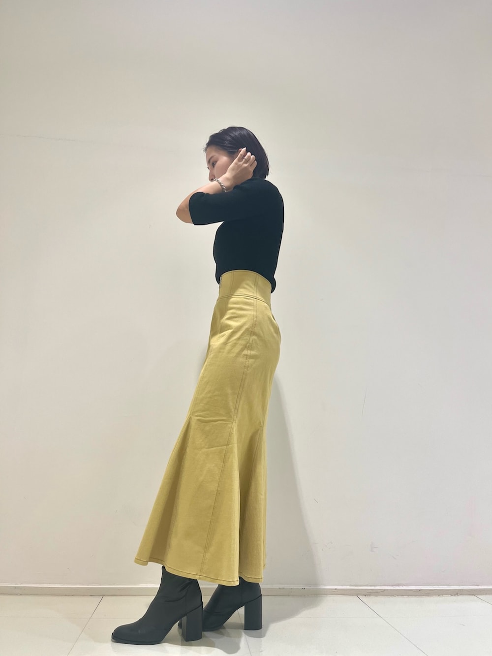 イエロー系のスカート、ブラック系のハンドバッグ、ブラック系のニット/セーターを着用したレディースの秋コーディネートの2枚目の写真