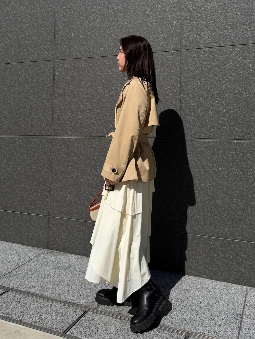 ベージュ系のトレンチコート、ホワイト系のスカート、ブラウン系のハンドバッグを着用したレディースの冬コーディネートの2枚目の写真