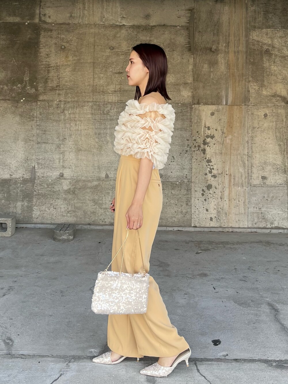 イエロー系のパンツドレス、ベージュ系のショルダーバッグ、ベージュ系のパンプスを着用したレディースの春コーディネートの2枚目の写真