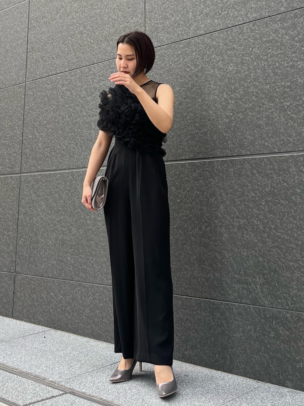 シルバー系のハンドバッグ、ブラック系のパンツドレス、シルバー系のパンプスを着用したレディースの春コーディネートの4枚目の写真