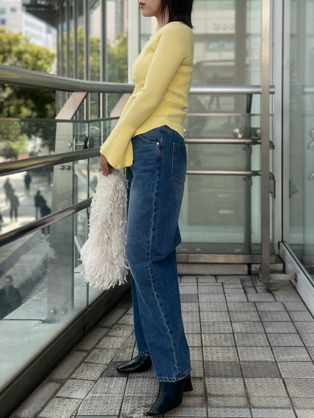 ブルー系のデニムパンツ、イエロー系のニット/セーター、ホワイト系のハンドバッグを着用したレディースの冬コーディネートの3枚目の写真