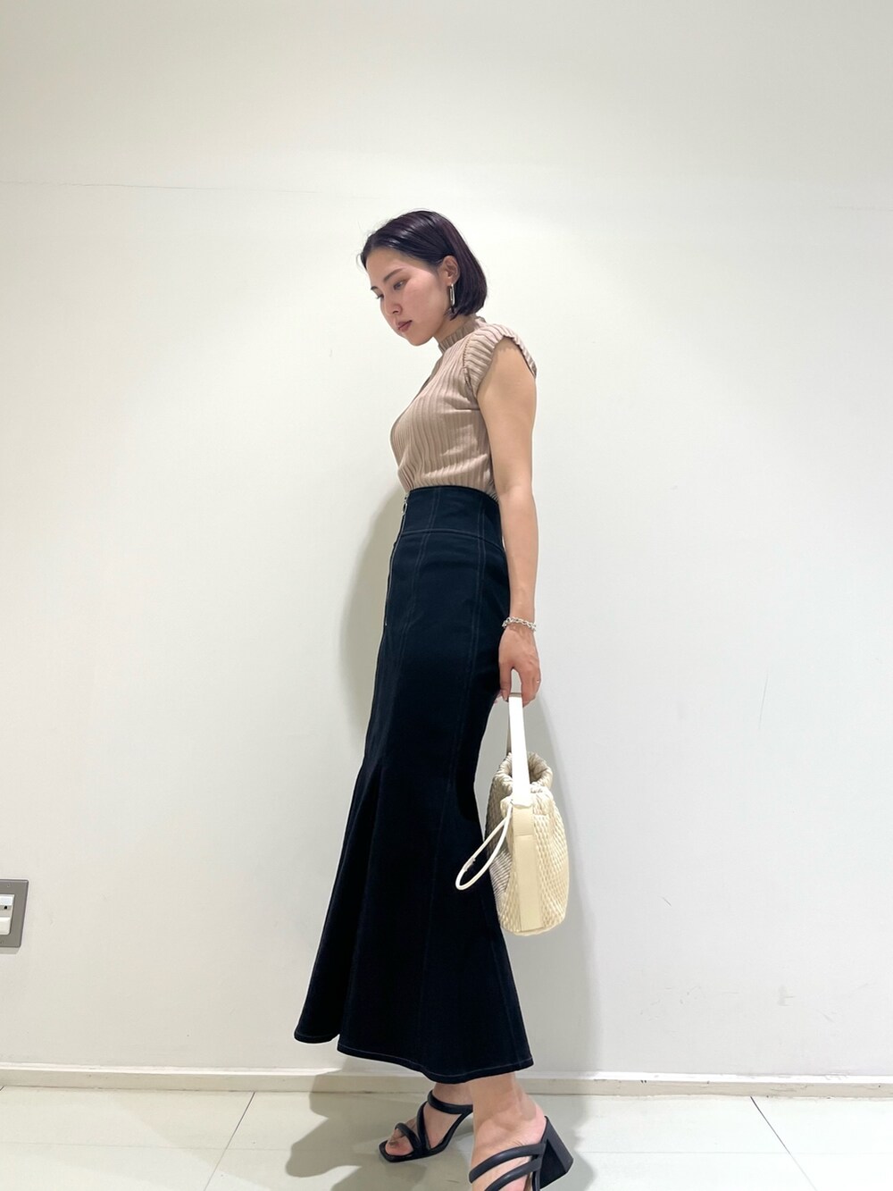 ブラック系のスカート、ベージュ系のニット/セーター、ホワイト系のハンドバッグを着用したレディースの夏コーディネートの4枚目の写真