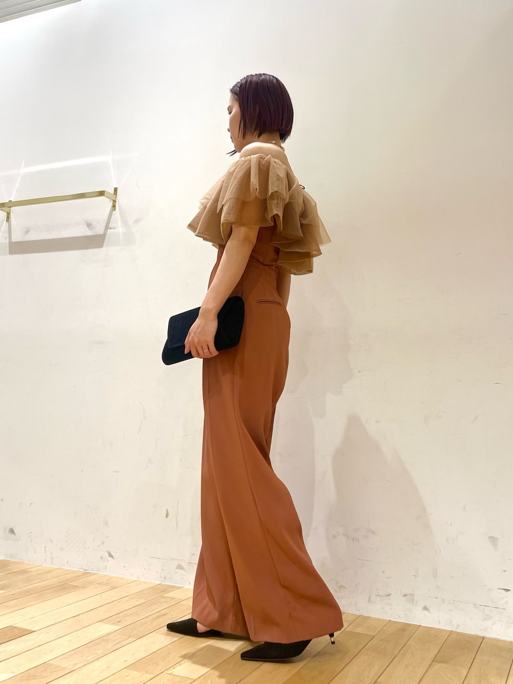 ブラック系のパンプス、オレンジ系のパンツドレス、ブラック系のクラッチバッグを着用したレディースの夏コーディネートの2枚目の写真