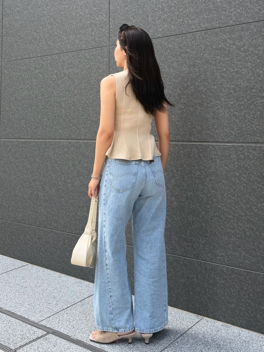 ブルー系のデニムパンツ、ベージュ系のニット/セーター、ホワイト系のハンドバッグを着用したレディースの夏コーディネートの3枚目の写真