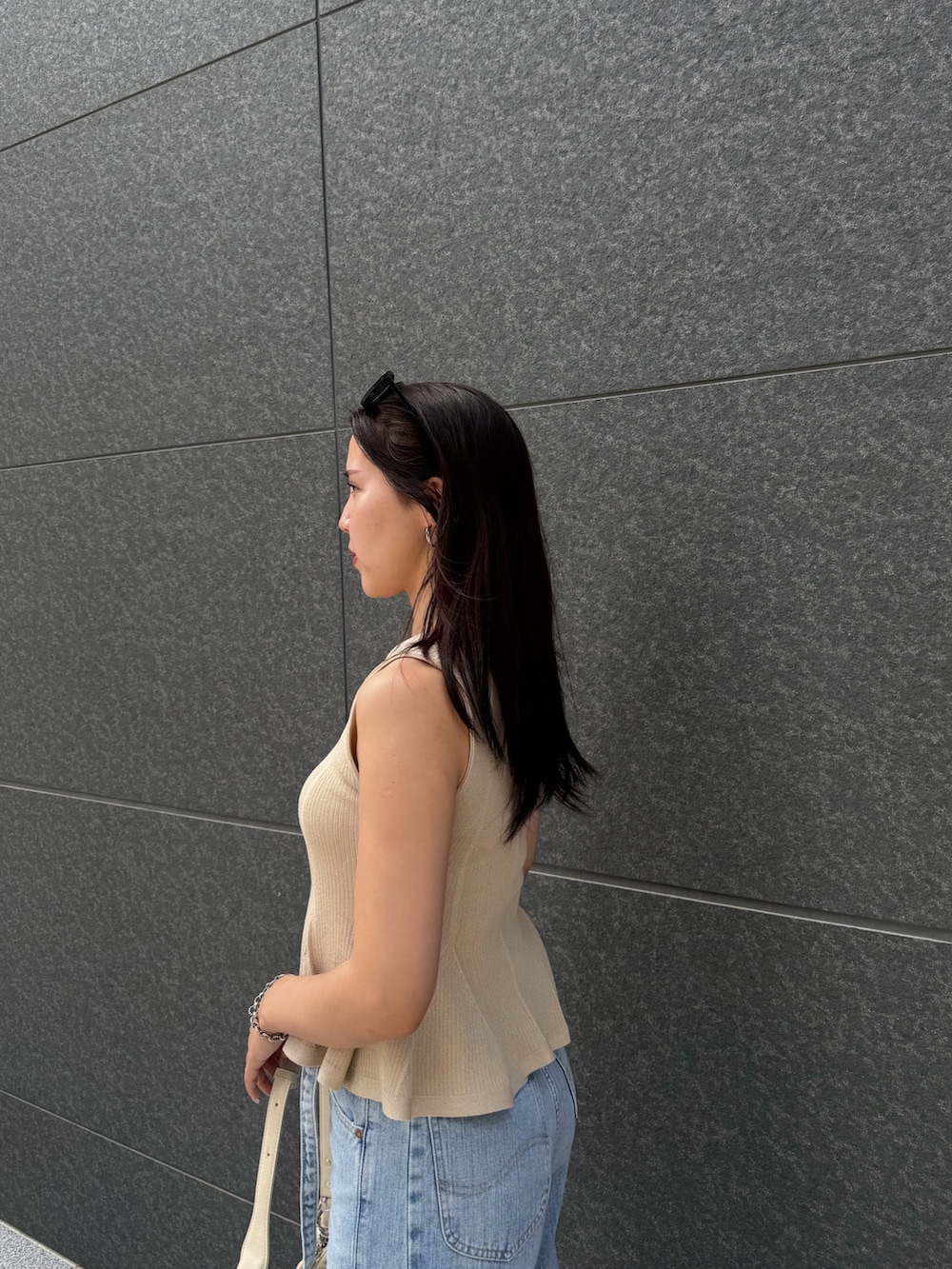 ブルー系のデニムパンツ、ベージュ系のニット/セーター、ホワイト系のハンドバッグを着用したレディースの夏コーディネートの5枚目の写真