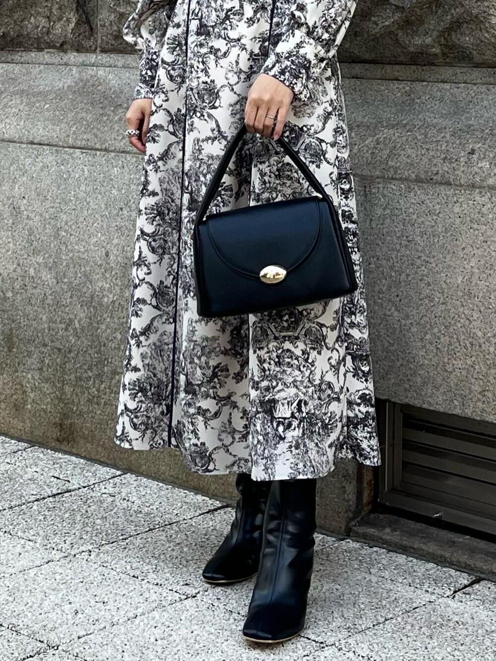 ホワイト系のワンピース、ブラック系のチェスターコート、ブラック系のハンドバッグを着用したレディースの冬コーディネートの7枚目の写真