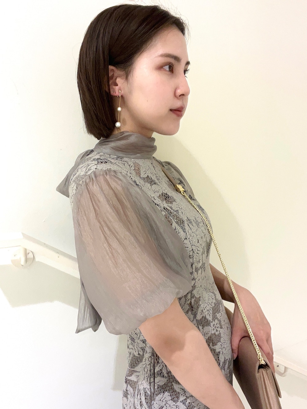 グレー系のドレス、ベージュ系のクラッチバッグ、ゴールド系のパンプスを着用したレディースの夏コーディネートの2枚目の写真