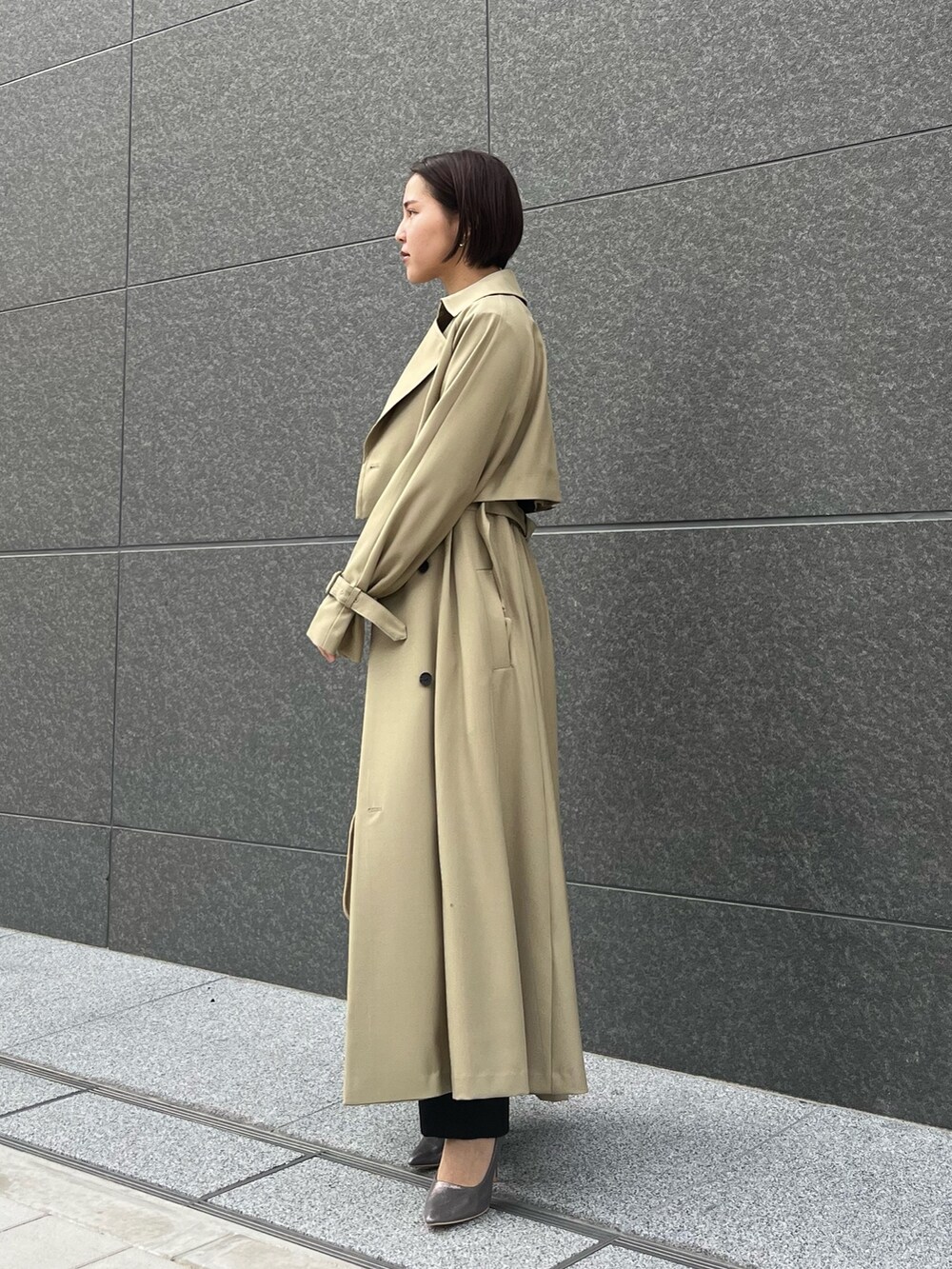 グリーン系のトレンチコート、シルバー系のパンプス、ブラック系のパンツドレスを着用したレディースの春コーディネートの2枚目の写真