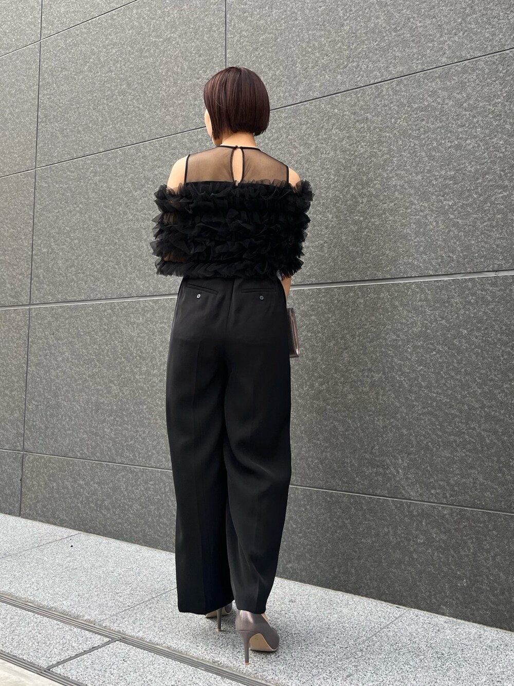 シルバー系のハンドバッグ、ブラック系のパンツドレス、シルバー系のパンプスを着用したレディースの春コーディネートの3枚目の写真