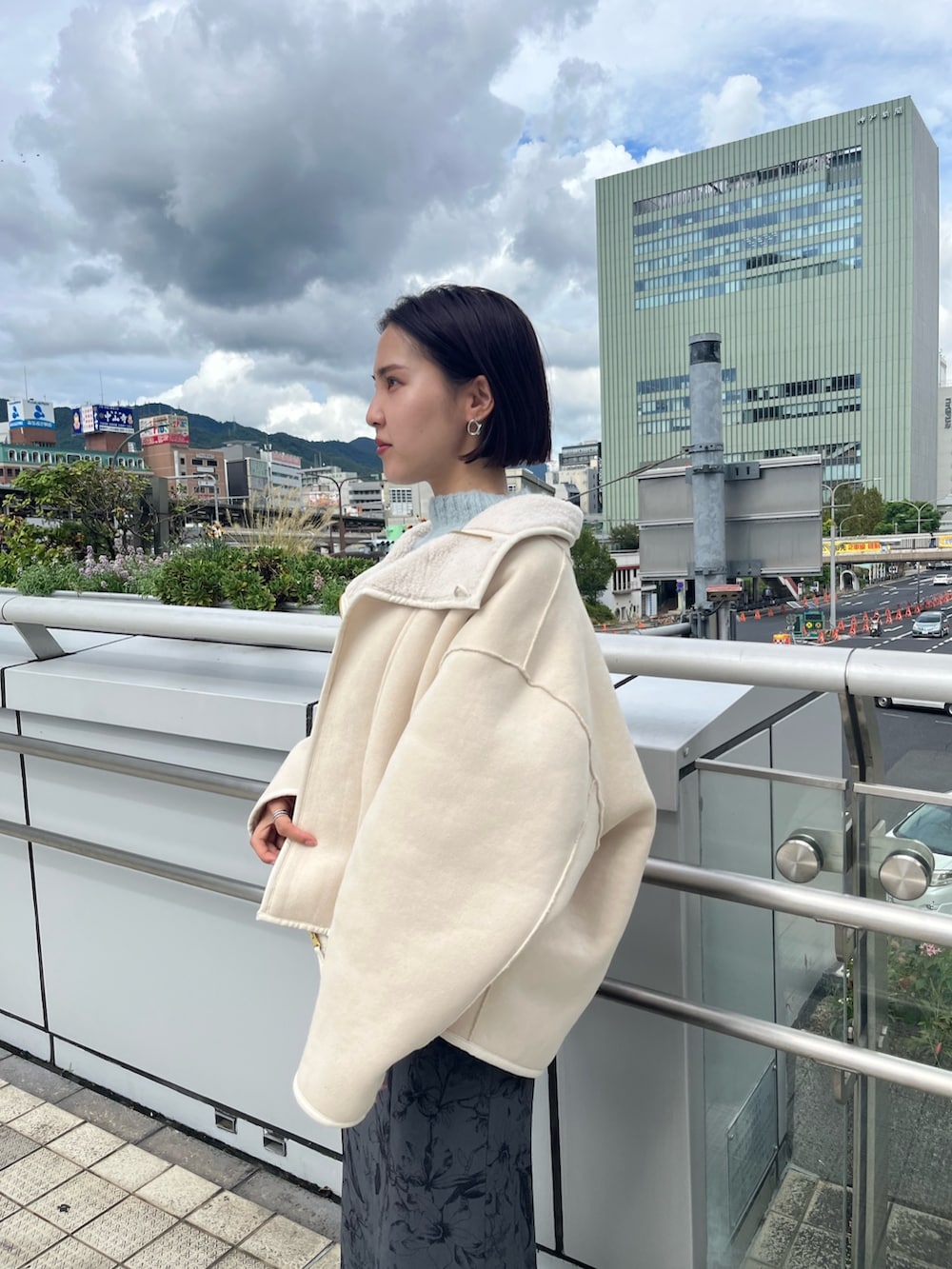 ホワイト系のムートンコート、グリーン系のニット/セーター、グレー系のスカートを着用したレディースの秋コーディネートの2枚目の写真