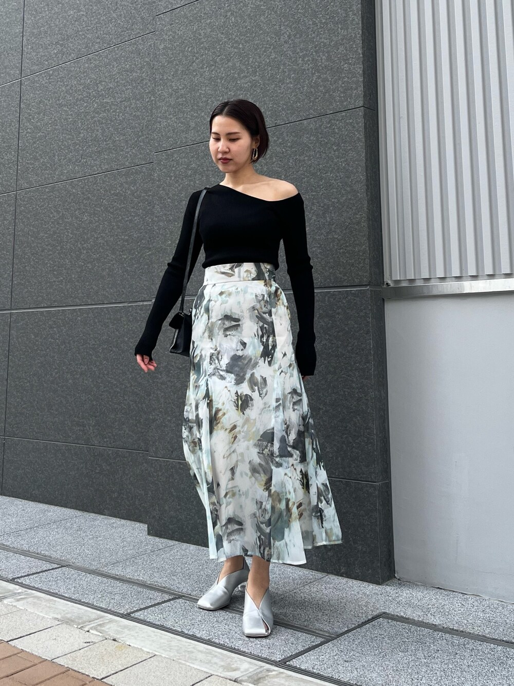 ブルー系のスカート、シルバー系のパンプス、ブラック系のハンドバッグを着用したレディースの春コーディネートの2枚目の写真