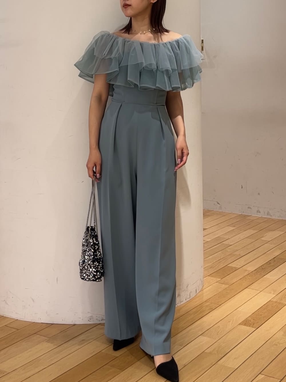 シルバー系のショルダーバッグ、ブラック系のパンプス、ブルー系のパンツドレスを着用したレディースの春コーディネートの5枚目の写真