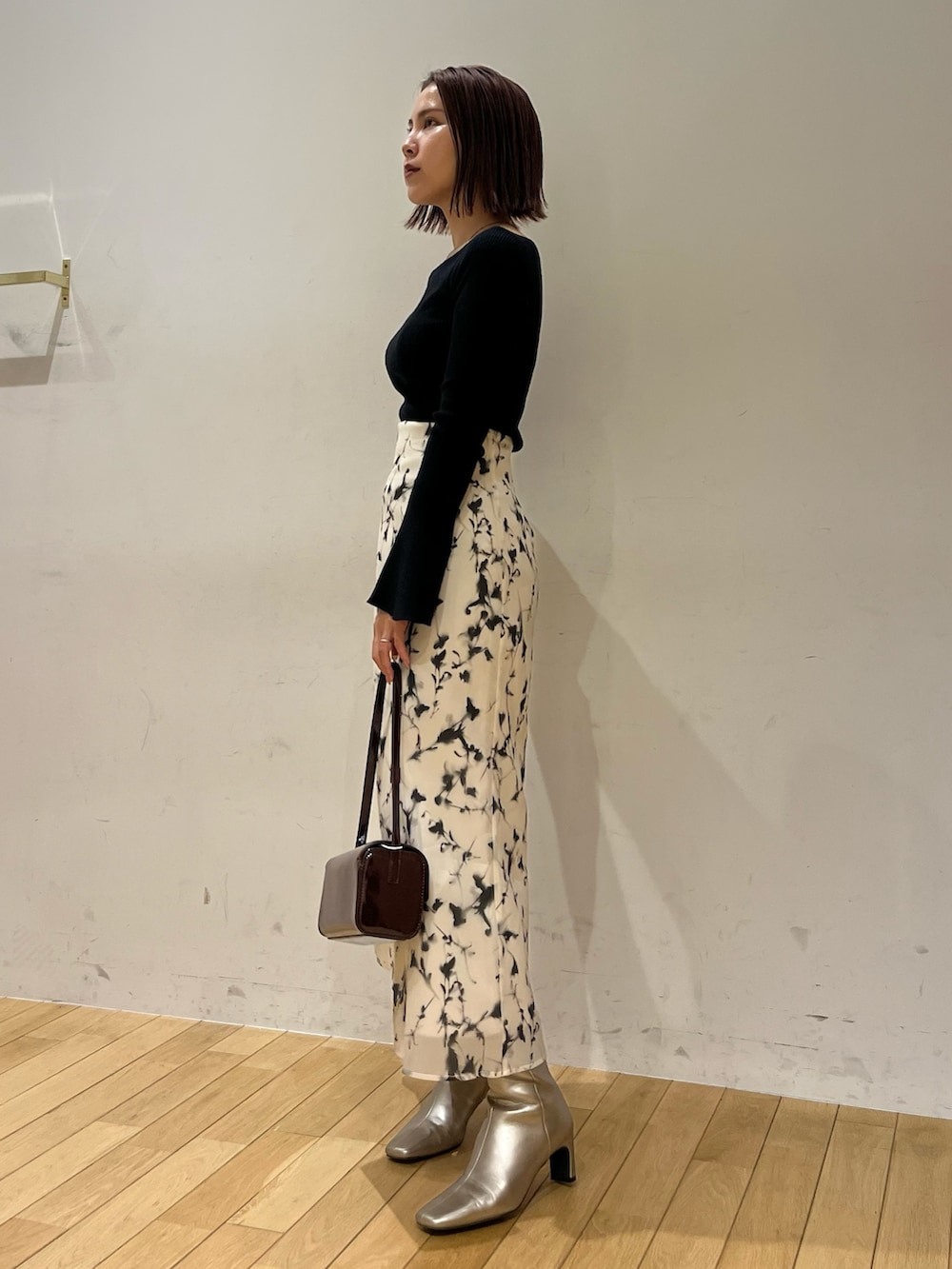 レッド系のショルダーバッグ、ホワイト系のスカート、シルバー系のブーツを着用したレディースの秋コーディネートの2枚目の写真