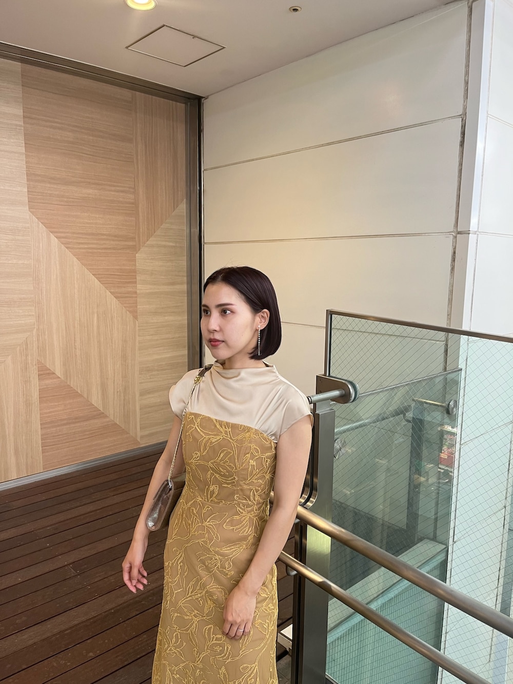 イエロー系のドレス、ブラウン系のパンプス、ゴールド系のハンドバッグを着用したレディースの夏コーディネートの3枚目の写真