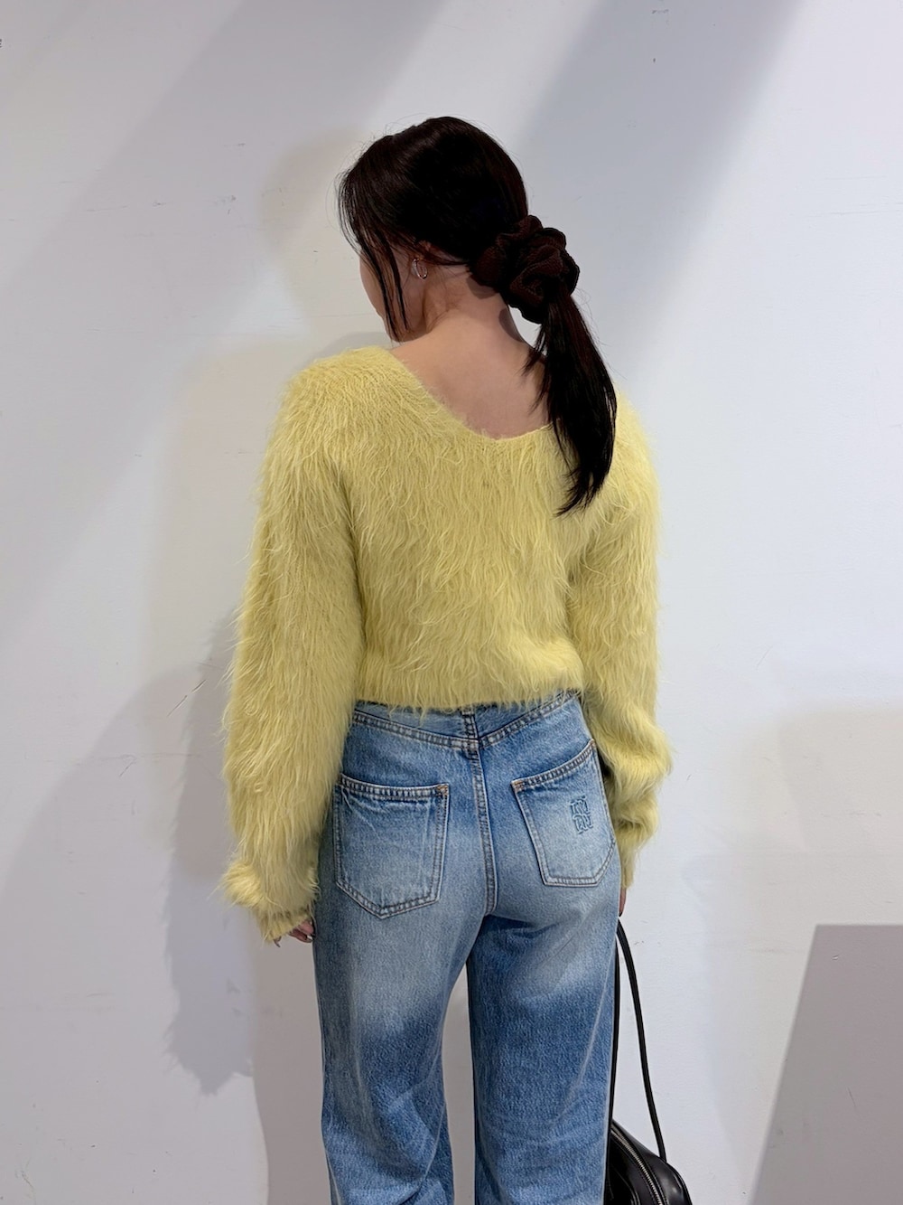 ブルー系のデニムパンツ、ブラック系のブーツ、イエロー系のニット/セーターを着用したレディースの秋コーディネートの5枚目の写真