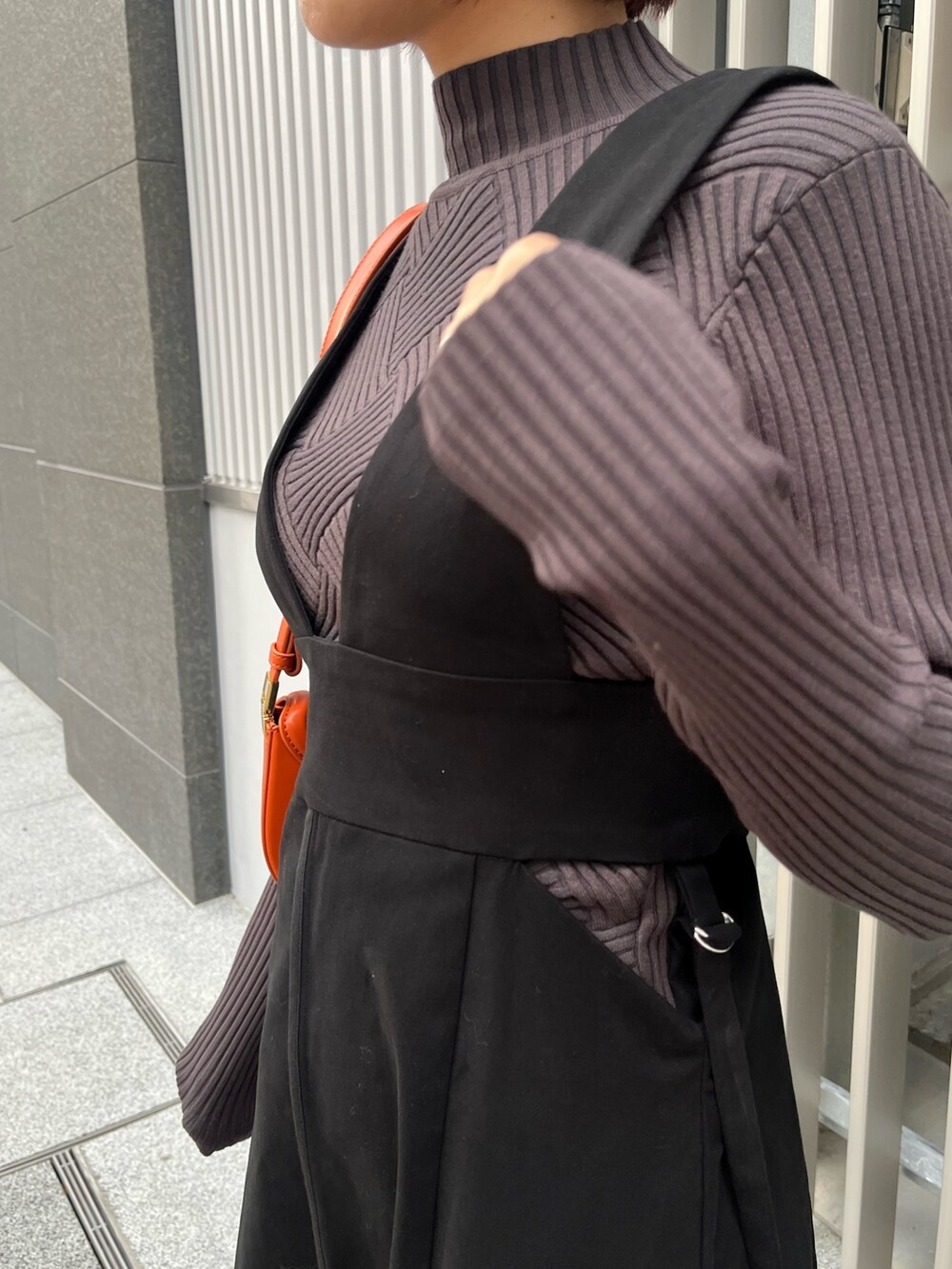 グレー系のニット/セーター、ブラック系のジャンパースカート、オレンジ系のショルダーバッグを着用したレディースの冬コーディネートの6枚目の写真