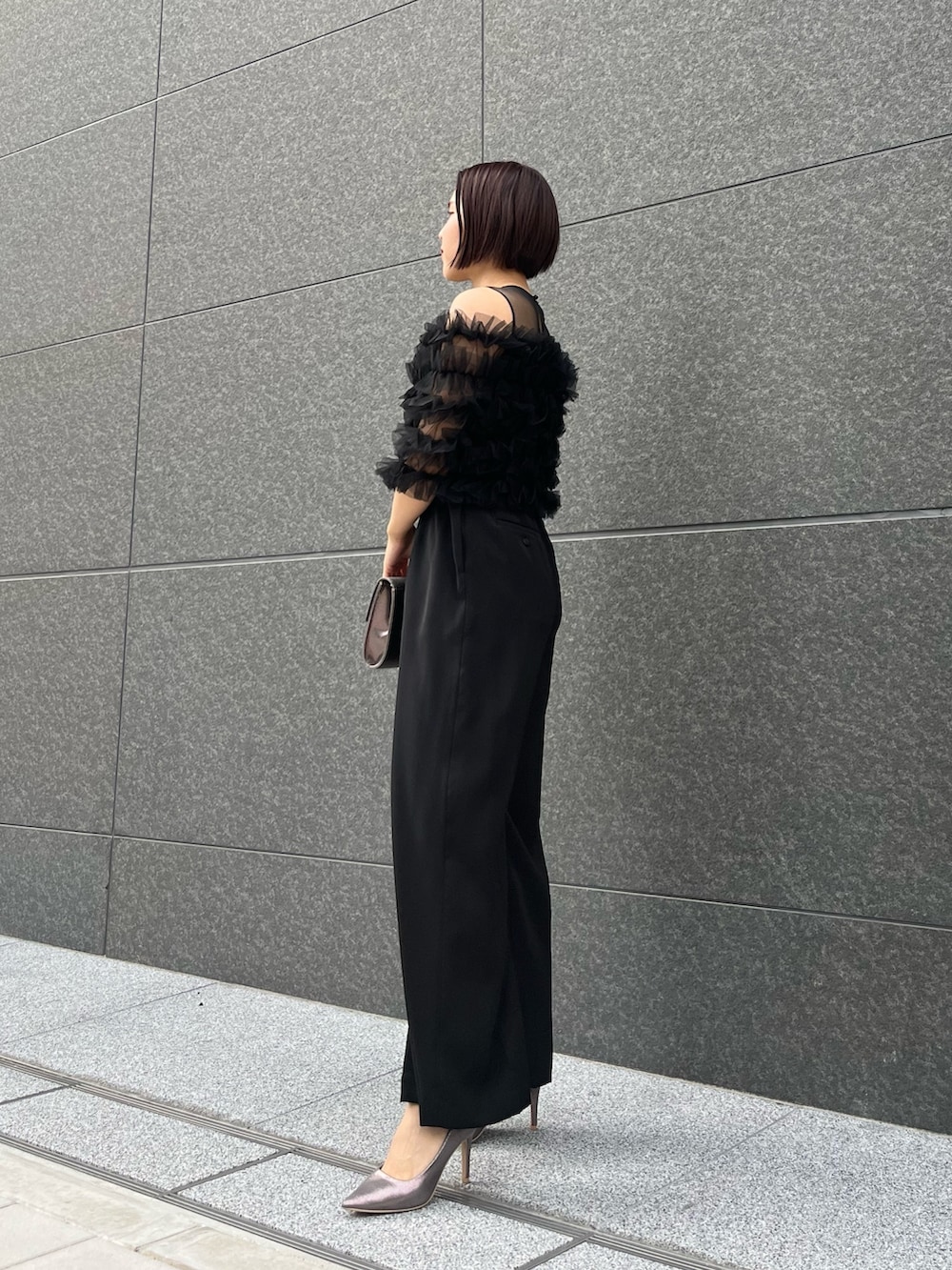 シルバー系のハンドバッグ、ブラック系のパンツドレス、シルバー系のパンプスを着用したレディースの春コーディネートの2枚目の写真