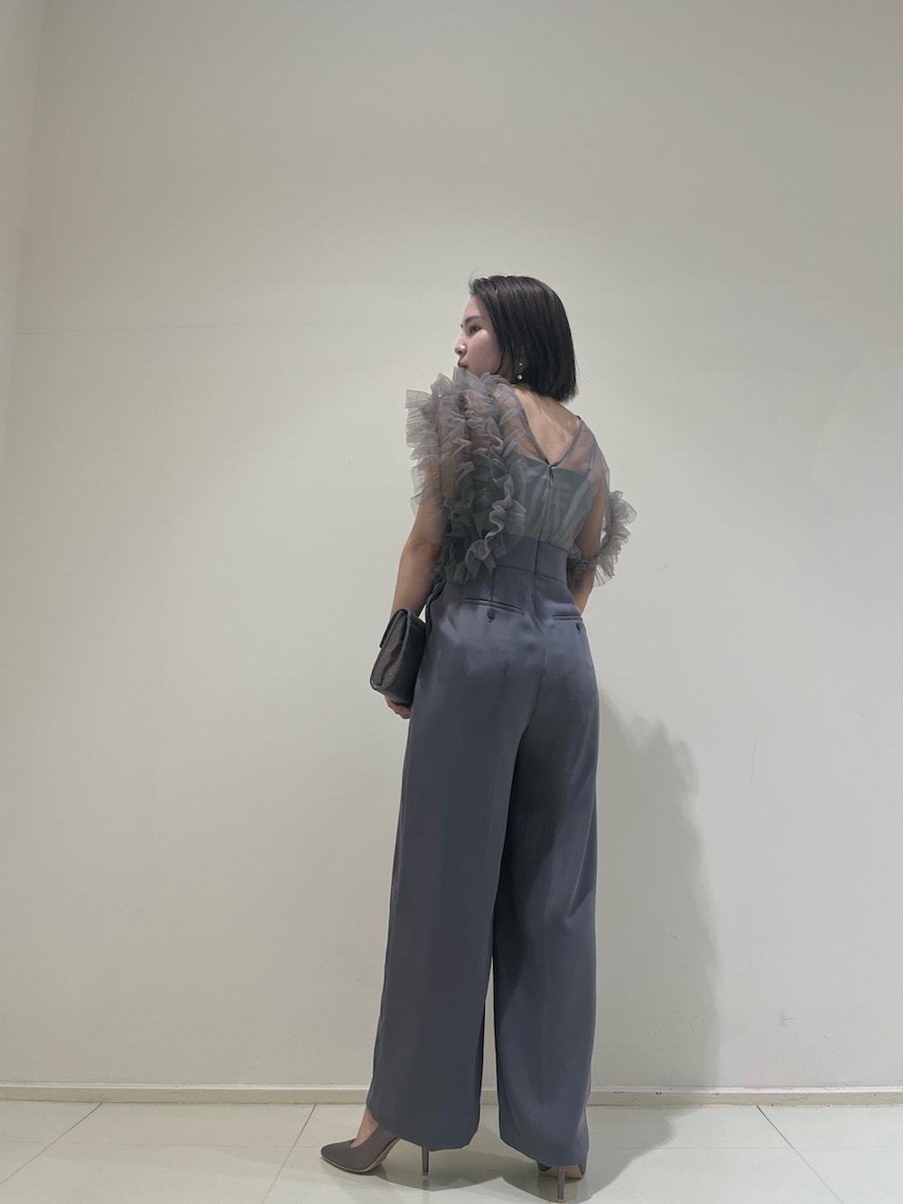 シルバー系のハンドバッグ、シルバー系のパンプス、グレー系のパンツドレスを着用したレディースの春コーディネートの4枚目の写真