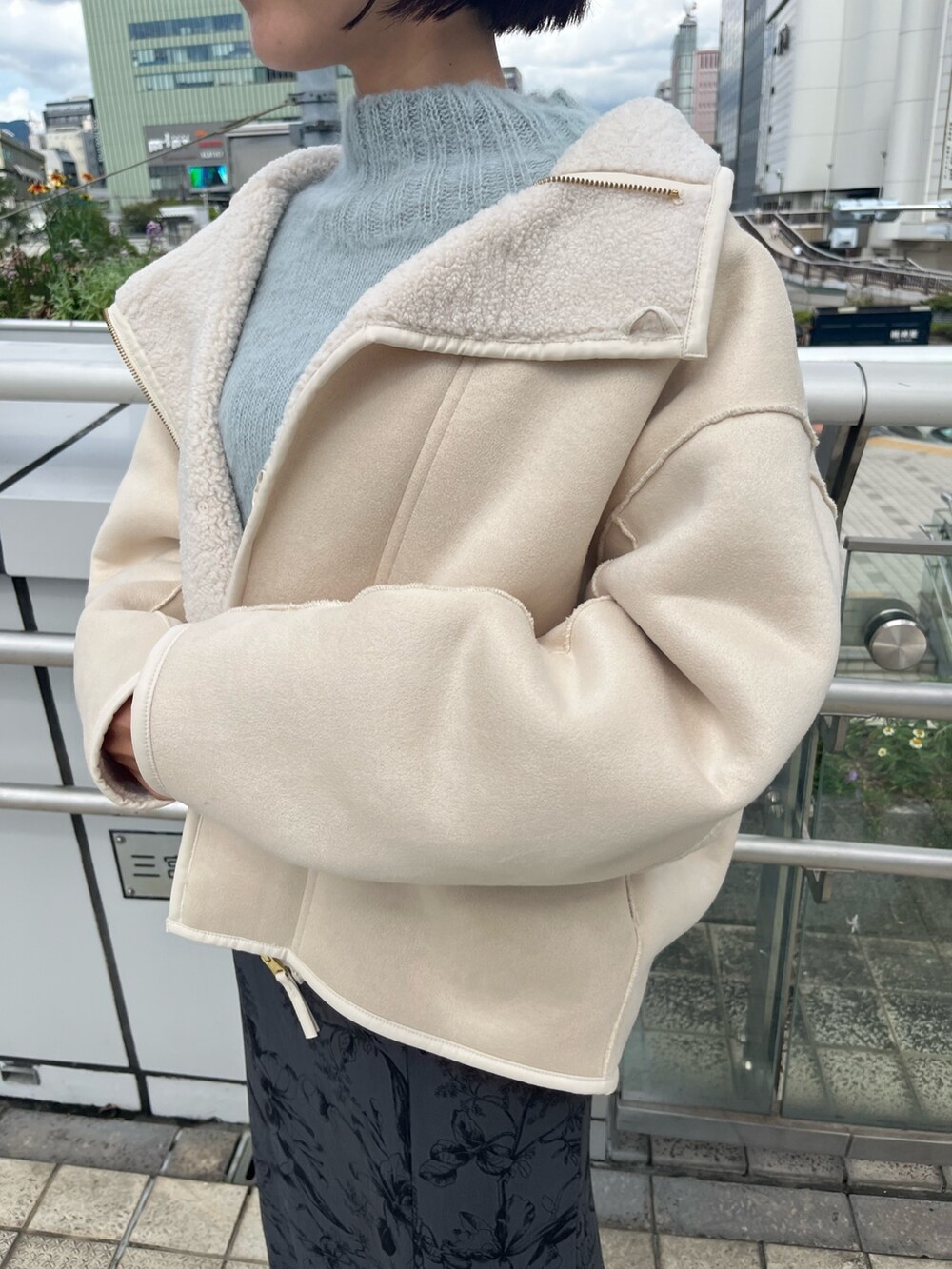 ホワイト系のムートンコート、グリーン系のニット/セーター、グレー系のスカートを着用したレディースの秋コーディネートの6枚目の写真