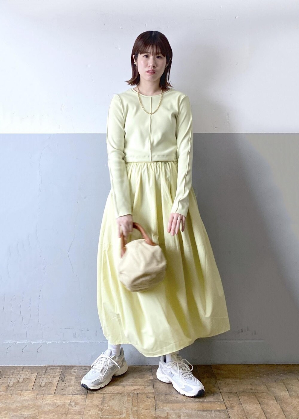 ホワイト系のハンドバッグ、イエロー系のワンピース、ゴールド系のネックレスを着用したレディースの春コーディネートの2枚目の写真