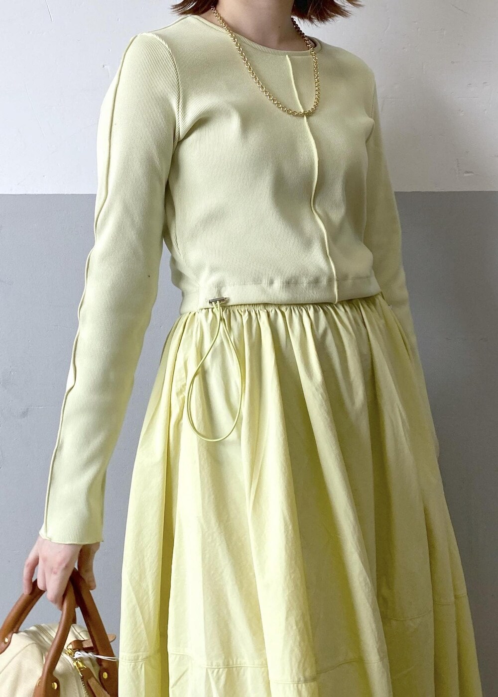 ホワイト系のハンドバッグ、イエロー系のワンピース、ゴールド系のネックレスを着用したレディースの春コーディネートの6枚目の写真