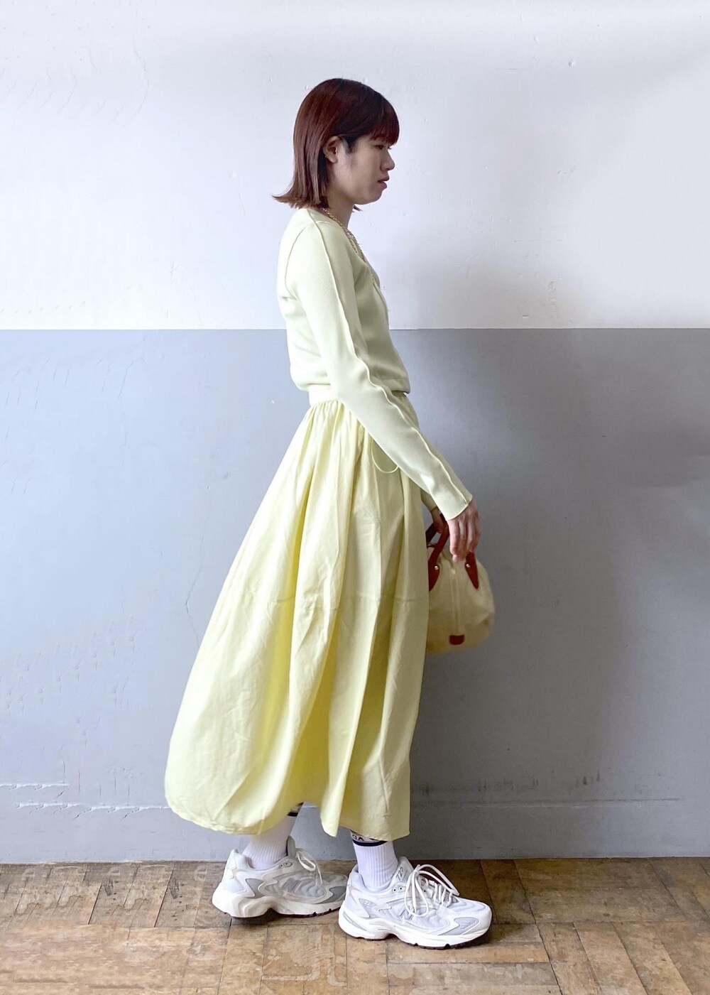 ホワイト系のハンドバッグ、イエロー系のワンピース、ゴールド系のネックレスを着用したレディースの春コーディネートの3枚目の写真