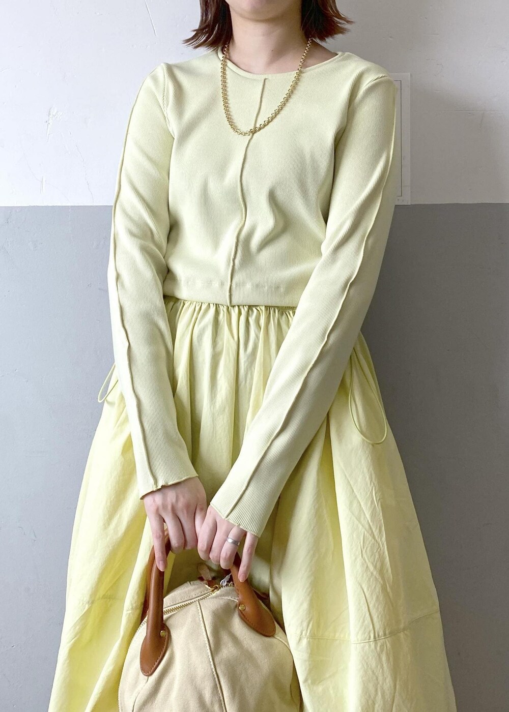 ホワイト系のハンドバッグ、イエロー系のワンピース、ゴールド系のネックレスを着用したレディースの春コーディネートの5枚目の写真