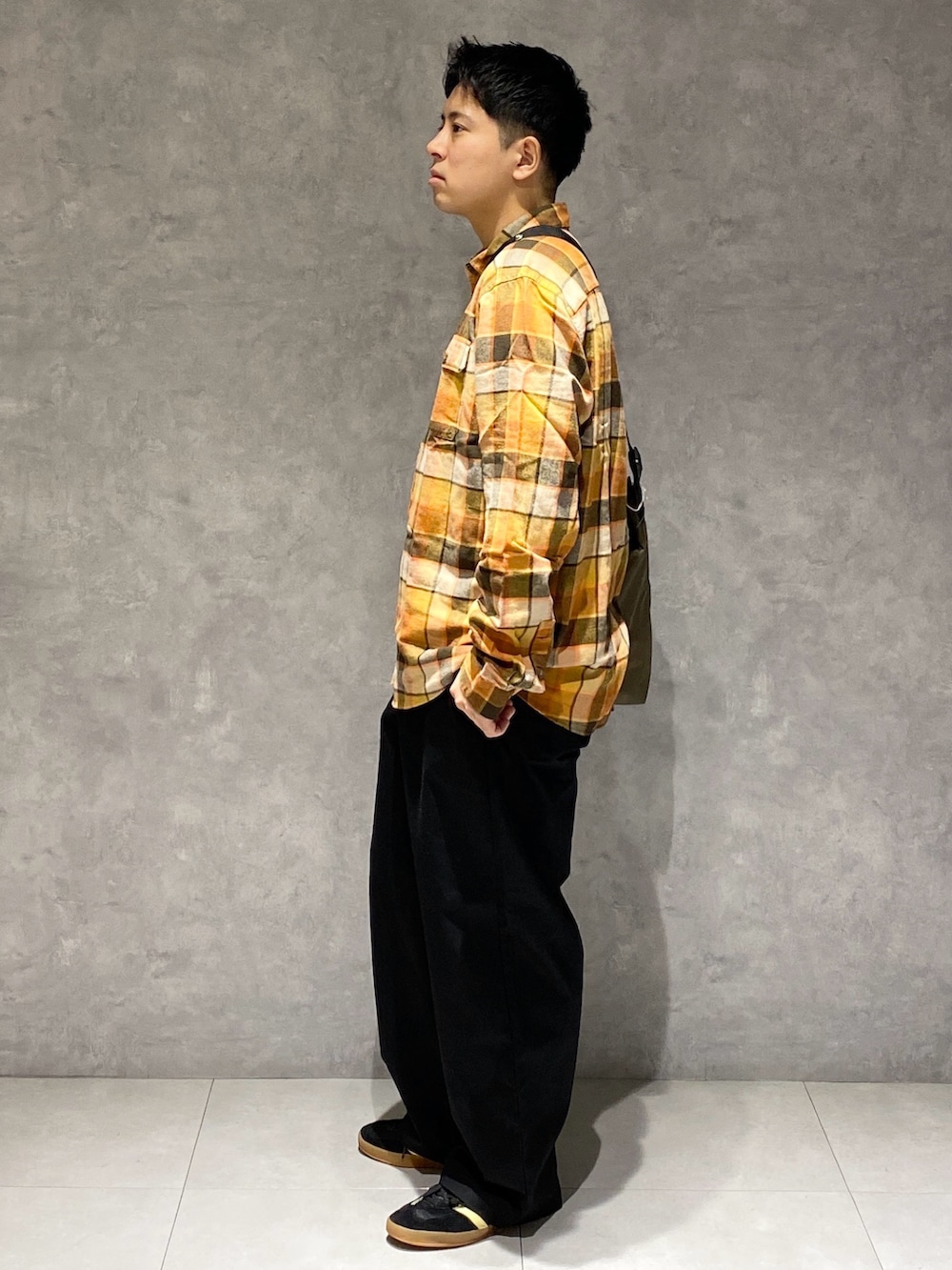 オレンジ系のシャツ/ブラウス、グリーン系のショルダーバッグ、ブラック系のチノパンツを着用したメンズの秋コーディネートの2枚目の写真