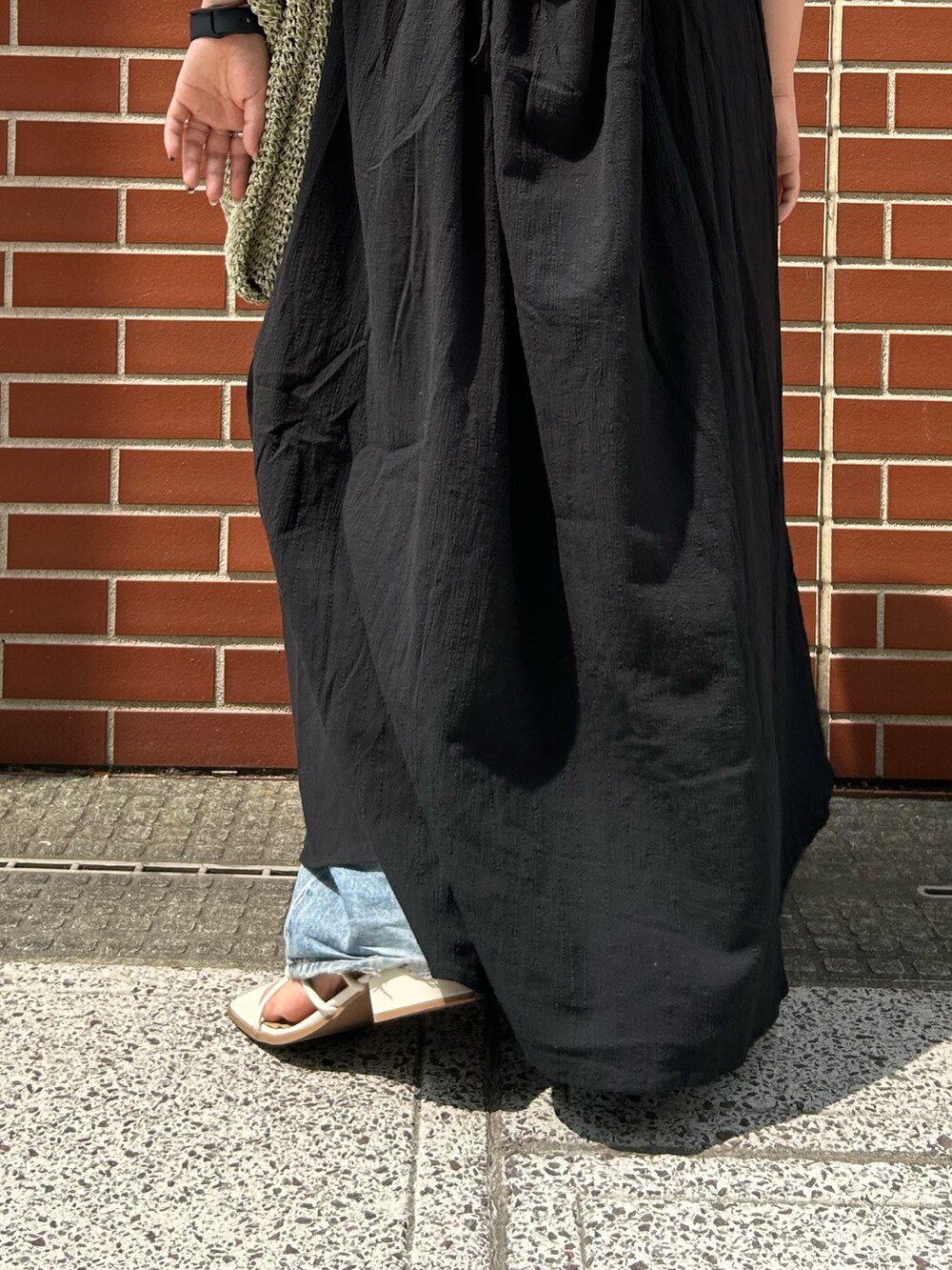 ブルー系のデニムパンツ、ブラック系のワンピース、グリーン系のショルダーバッグを着用したレディースの夏コーディネートの6枚目の写真