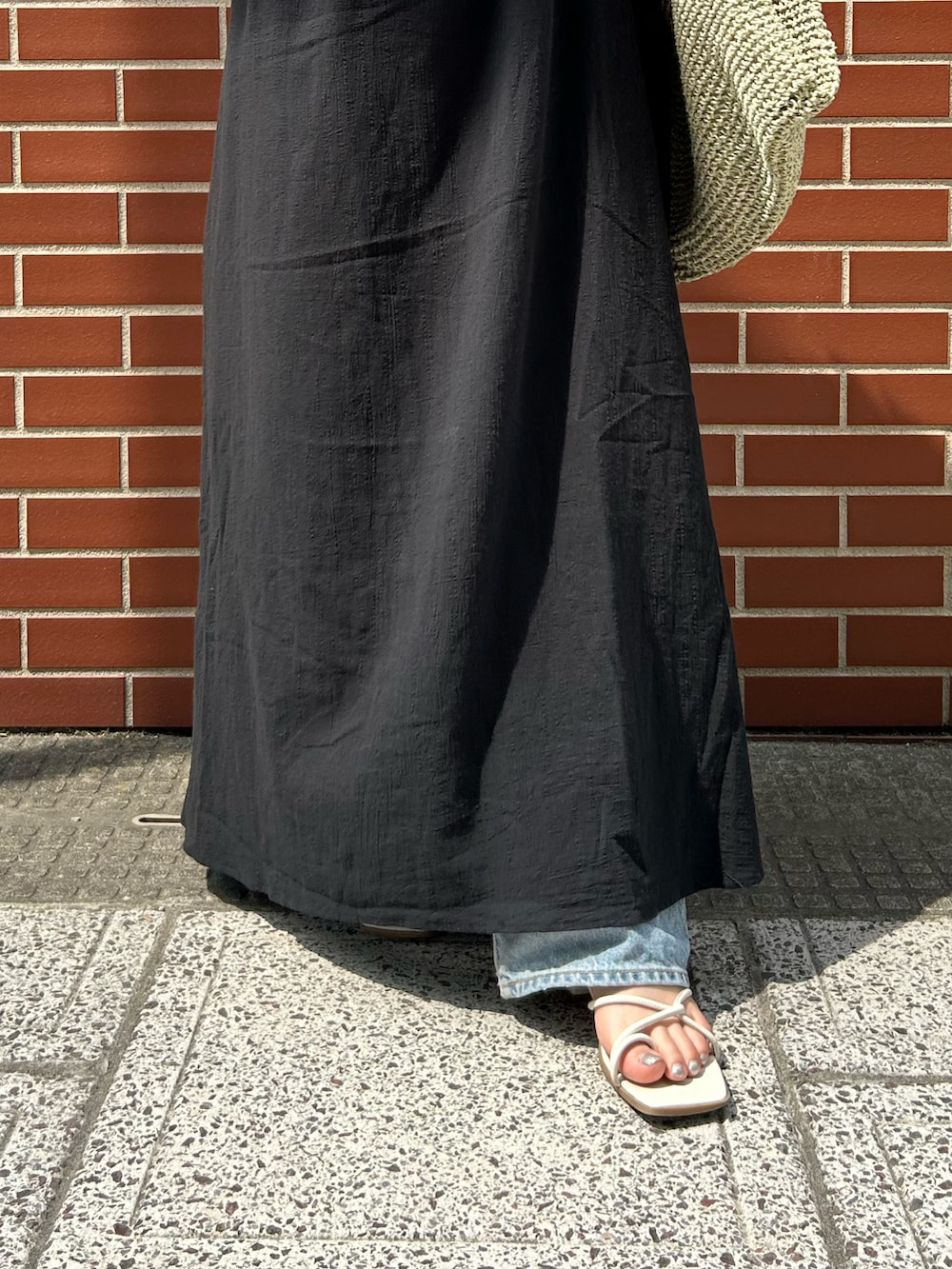 ブルー系のデニムパンツ、ブラック系のワンピース、グリーン系のショルダーバッグを着用したレディースの夏コーディネートの4枚目の写真