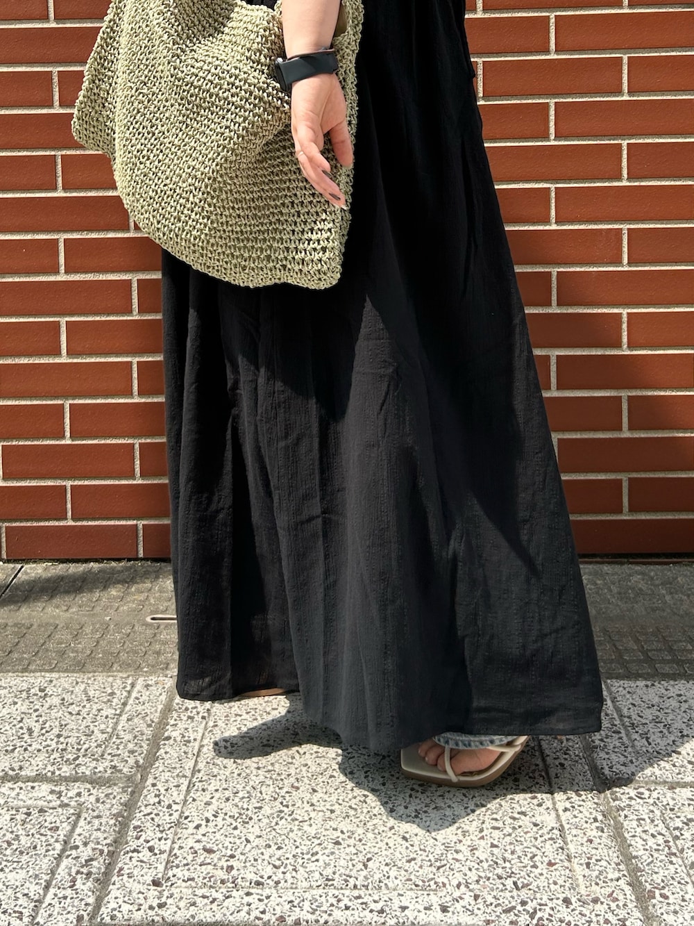 ブルー系のデニムパンツ、ブラック系のワンピース、グリーン系のショルダーバッグを着用したレディースの夏コーディネートの5枚目の写真