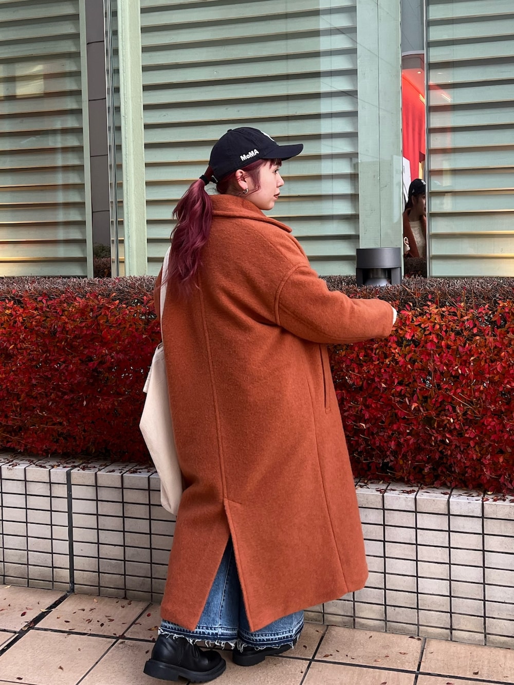 オレンジ系のチェスターコート、ホワイト系のニット/セーター、ブルー系のデニムパンツを着用したレディースの冬コーディネートの3枚目の写真