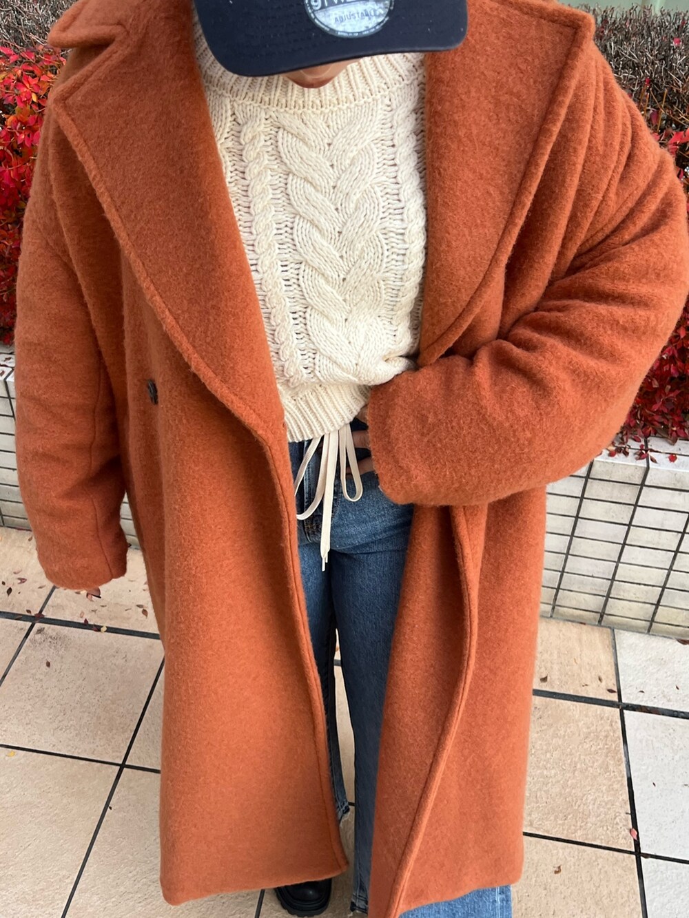 オレンジ系のチェスターコート、ホワイト系のニット/セーター、ブルー系のデニムパンツを着用したレディースの冬コーディネートの4枚目の写真