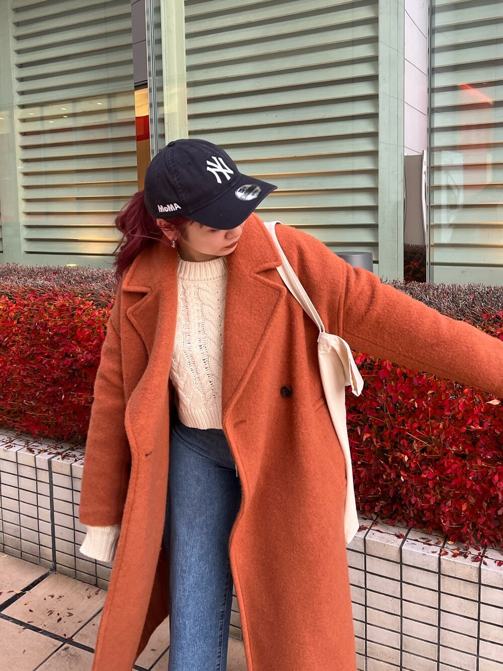 オレンジ系のチェスターコート、ホワイト系のニット/セーター、ブルー系のデニムパンツを着用したレディースの冬コーディネートの2枚目の写真