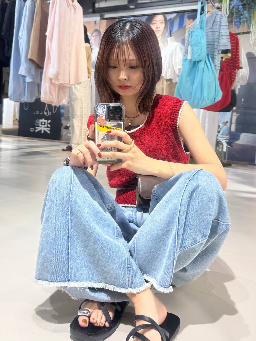 ブルー系のデニムパンツ、ブラック系のサンダル、レッド系のベストを着用したレディースの春コーディネートの7枚目の写真