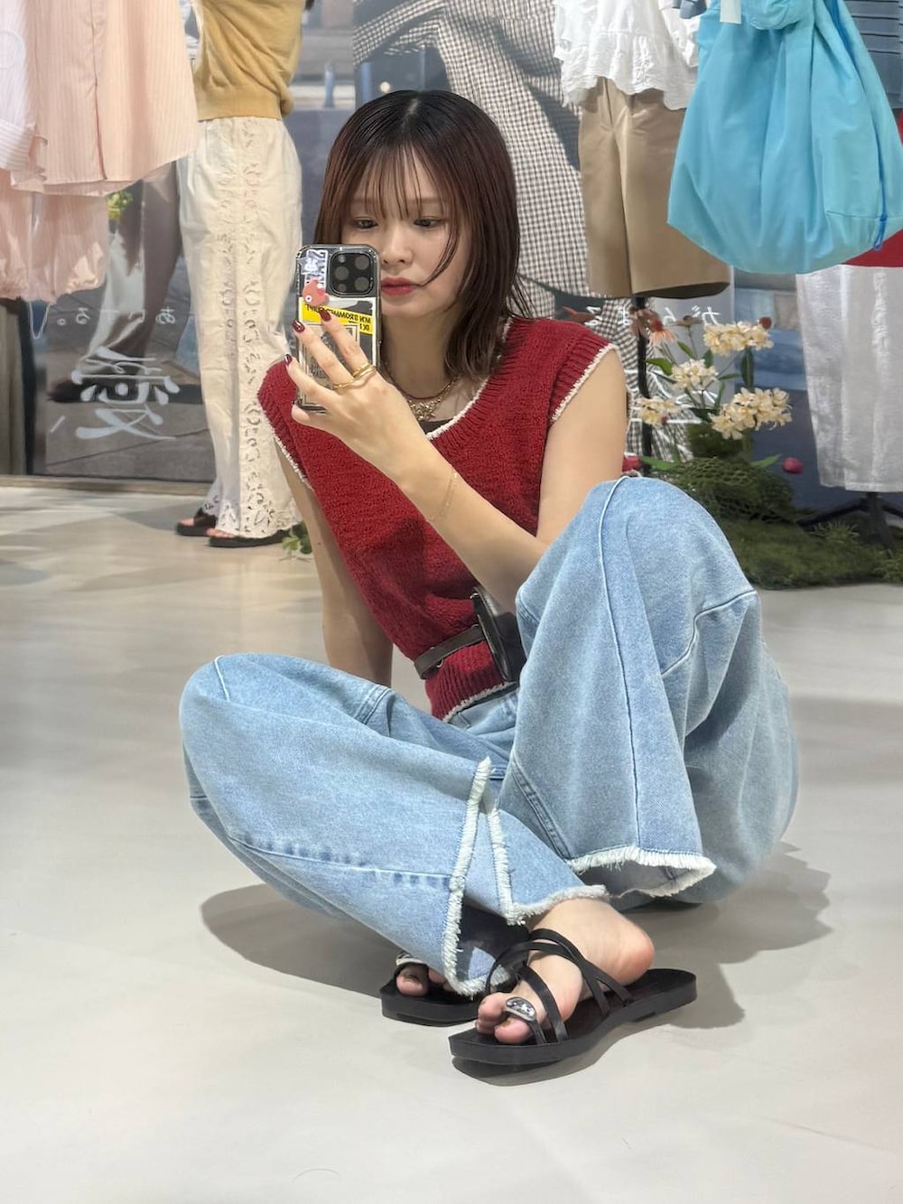 ブルー系のデニムパンツ、ブラック系のサンダル、レッド系のベストを着用したレディースの春コーディネートの6枚目の写真